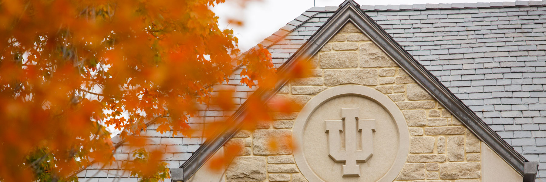 The IU trident on a campus building surrounded by Fall leaves